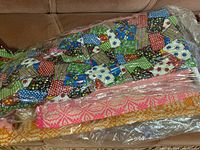 Packaged vintage linens with patchwork quilt comforter visible on top and other woven blankets underneath.