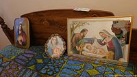 Framed mirrored Nativity picture, bedside lamp with Madonna image, and two smaller Jesus pictures on bed