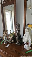 Photo showing entire lot of religious figurines on wooden dresser, including ceramic Madonna, ceramic girl holding cross, nativity scene figures, Jesus on cross, and glass children playing figurine.