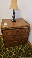 Front view of wood laminate two drawer side table with black lamp on top.