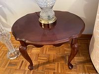 Close-up image of one wooden side table showing scalloped beveled edges on table top and curved cabriole legs