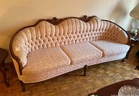 Front view of vintage sofa featuring floral motif upholstery, wooden frame with carved details, and three seat cushions with slight stain on one.