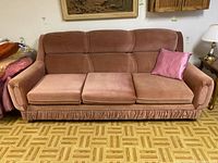 Front view of the pink upholstered sofa with three seat cushions and one pink pillow on wooden parquet flooring.