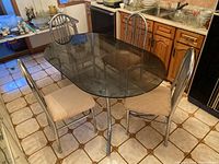 Dining table with oval smokey glass top and four chairs arranged around it, showing table and chair details.