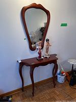 Wood entry table with beveled edges, carved legs, and a wall-mounted scalloped wood framed mirror above. The table measures approximately 42 inches wide, 14 inches deep, and 31 inches tall. The mirror measures approximately 27 by 39 inches.