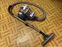 Full view of Bissell vacuum cleaner with hose, metal extension wand, and floor nozzle attachment placed on a wood-patterned floor.