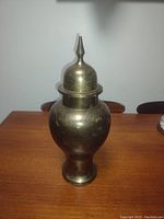 Front view of the brass urn on a wooden table, showing its overall shape and finish.