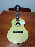 Full top view of the children's acoustic guitar showing cream-colored body front, six strings, black bridge and fretboard, and attached lot number 80 card.
