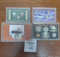 Photo showing four collectible coin sets in plastic cases placed on wooden surface, including Titanic, U.S. Monuments, Mercury Dime Mint Mark, and Favorite Coins Last Century sets.