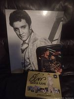 Photo showing large black and white Elvis Presley photo, small black Elvis performance tin, and Elvis Trivia Game box