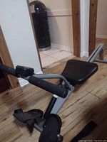 Rowing machine showing padded seat, frame, and foot pedals with straps on wooden floor.