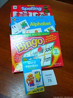 Photo showing four educational literacy games including Spelling puzzle, Alphabet cards, Sight Words Bingo, Word Families flash cards on a wooden surface