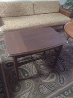 Full view of wooden side table in front of sofa showing top surface and leg structure.