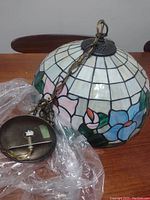 Side view of the pendant light shade showing floral mosaic pattern and the hanging hardware with electrical cord and chain.