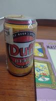 Duff Beer can replica with yellow and red label, taped at the top, showing wear.