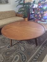 Front view of round teak coffee table showing top surface and three legs in living room setting
