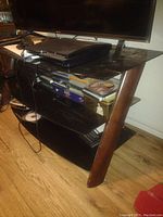 TV stand with glass shelves and wood legs, holding electronics and media items.