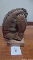 Front view of a brown leather vintage baseball first baseman glove on a wooden display stand, showing the curved padded mitt and lacing details.