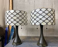 Front view of both lamps side by side on metal shelf against cinder block wall