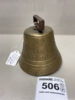 Front side of brass cowbell showing '1878 Vignobel' embossed with rusted iron handle on top.