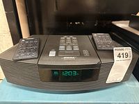Front view of Bose Wave Radio/CD player showing digital clock display and two remotes on top.