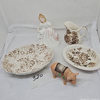 Full grouping of collectibles showing Royal Doulton girl figurine, three brown floral transferware pieces, and Perillo pig figurine arranged together.