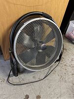 Front view of the industrial floor fan showing protective grille, blades, and metal frame. Dust visible on the fan.