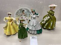 Four vintage lady ceramic figurines displayed together with a Limoges plate behind