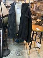 Front view of the black Levi's jacket draped over the white mannequin torso on a chrome stand. Shows the front pockets and zipper.