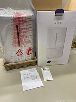 Miko Myst humidifier in protective plastic wrap inside packaging fiber tray next to damaged box and instruction manual.
