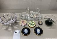 Clear cut glass perfume bottles with stoppers on cut glass tray, along with framed circular cameos and compact mirrors in various classical artwork styles, plus a clear flared glass bowl and art glass paperweight with green bubbles.