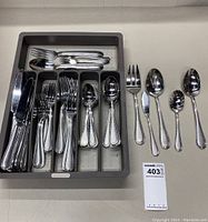 Photo showing the full set of flatware in organizer tray, including dinner knives, dinner forks, tablespoons, teaspoons, and some serving utensils laid out next to the tray.