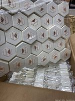 Box of hexagonal Moricci jewelry boxes tightly shrink wrapped in plastic and stacked in columns inside a large cardboard box.