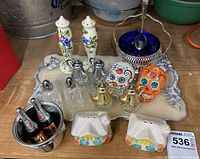 Full lot displayed on wooden surface showing all salt and pepper shakers, tray, and small buckets with bottles.