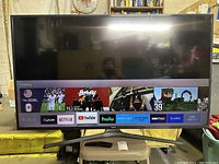 Front view of TV powered on, showing home screen with streaming app icons