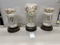 Overall photo of the set showing one taller lamp flanked by two smaller lamps on brown bases with hanging crystals and gilded designs.