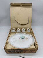 Photo of open vintage snack set box showing four white milk glass cups with handles and one floral designed snack plate on top.