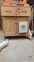 Front view of small wood cabinet with drawer and double doors. Celcy first aid kit mounted on door. Ridgid machine visible on cabinet top (not included).
