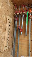 Four metal pipe clamps hanging vertically on a wall with wooden boards behind them