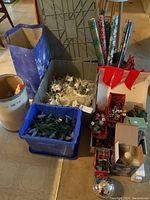 Photo showing bins and bags filled with Christmas light strands, Thomas Kinkade village pieces, and rolls of wrapping paper.