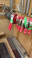 Metal clip clamps with red handles and metal bodies hung on wall.