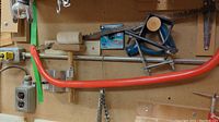 Two 16-inch blue metal pipe clamps, large orange bow saw, and wooden-handled rubber mallet hung on a pegboard.