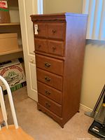 Front view of tall wooden dresser with six drawers and metal handles, placed in a room corner.