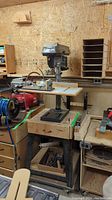 Full view of the Delta drill press mounted on a sturdy wooden block and base with surrounding workshop items.