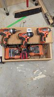 Three Ridgid cordless drills with batteries, two battery chargers, small set of bits, all stored inside a wooden box.