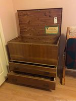 Front view of open heirloom cedar chest showing empty interior and two open bottom drawers.