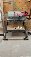 Full view of Delta jointer on metal stand with dust pan, hand broom and push blocks visible on top and shelf