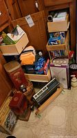 View of boxes, partial rolls, tins, towels, and other items stacked near cabinetry on floor