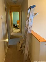 Photo showing aluminum step ladder leaning against wall in hallway, full length visible