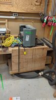 Planer mounted on wooden cabinet with casters, hoses and extension cord visible